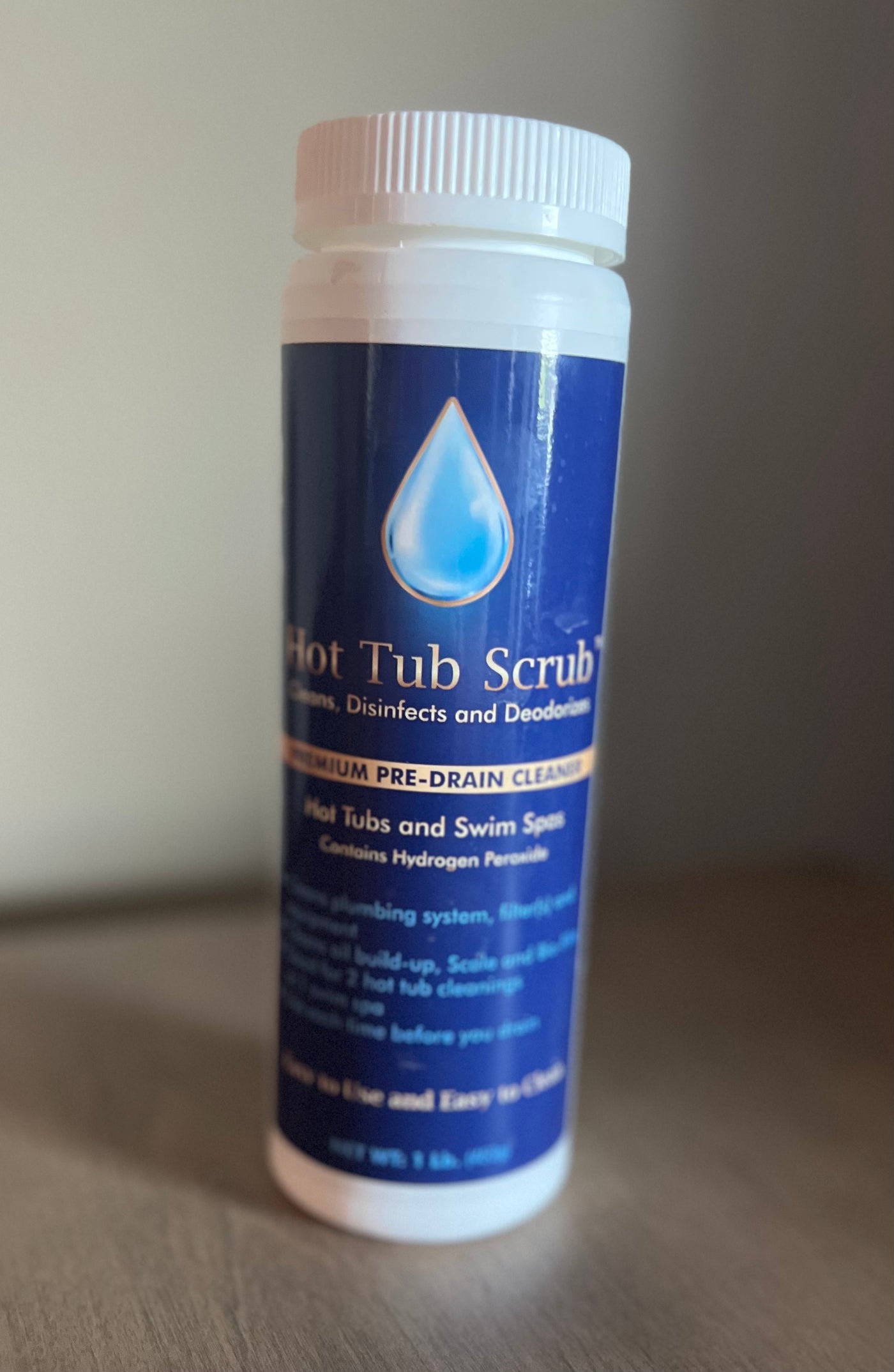 A bottle of  Hot Tub  Scrub sitting on a table  it is a blue lable with gold lettering and a blue water droplet